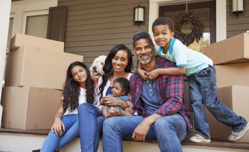 African American family sitting on the steps of their new home with boxes