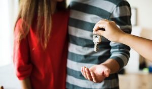 Woman in red shirt and man in green stripes receiving keys to their new home