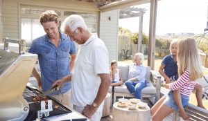 Young and older man grilling and having a picnic on a patio with family