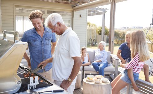 Young and older man grilling and having a picnic on a patio with family