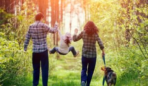 family with child and dog walking through wooded area
