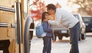 father kissing young daughter as she's getting on school bus
