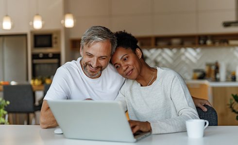 couple sitting in kitchen looking at laptop