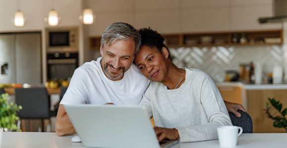 couple sitting in kitchen looking at laptop